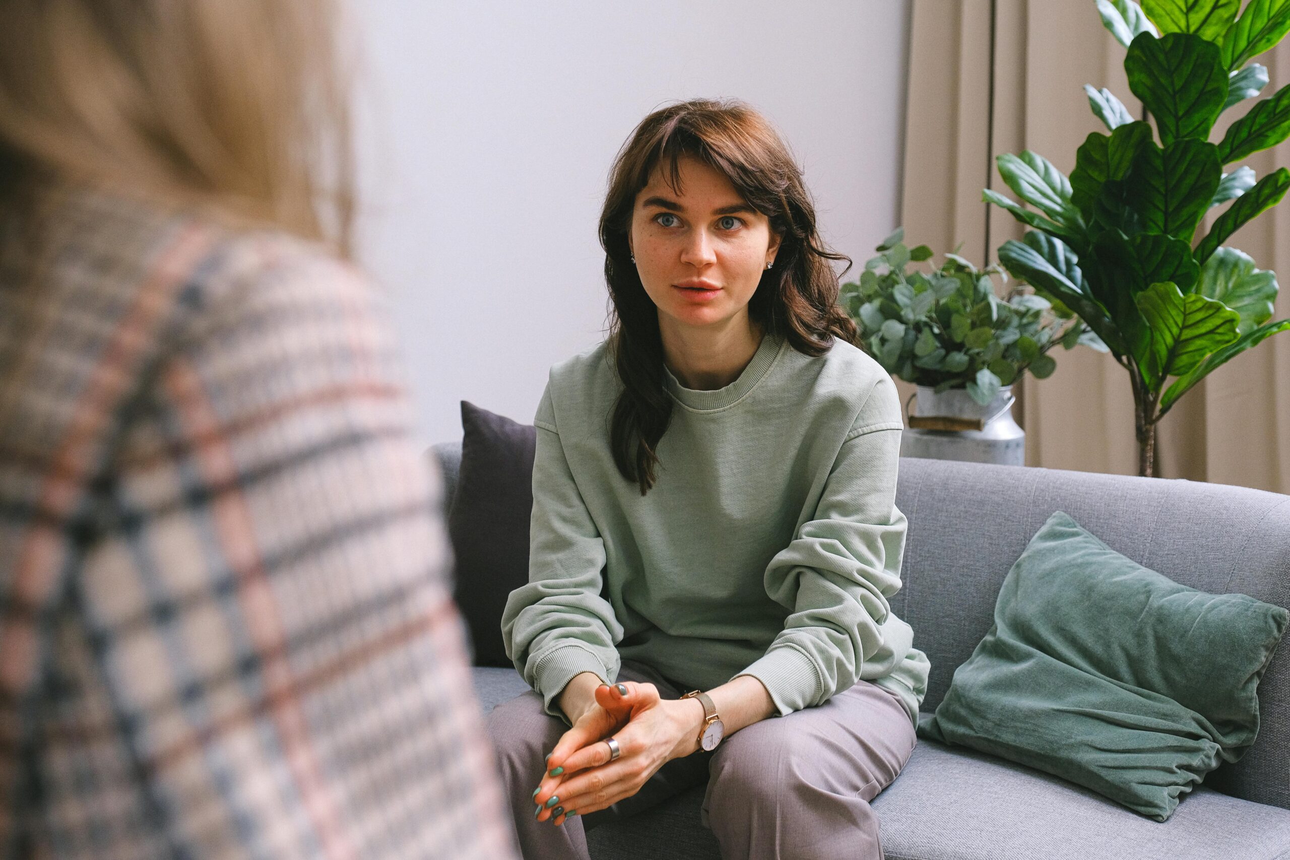 A focused woman during a therapy session, seated on a sofa indoors.